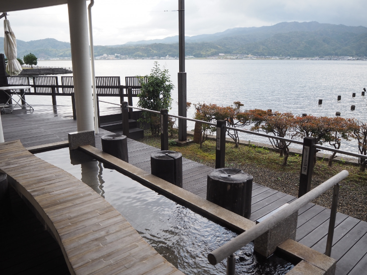 天橋立温泉的露天足湯，背後是一望無際的海景和遠處的山脈，提供放鬆和享受大自然的體驗。