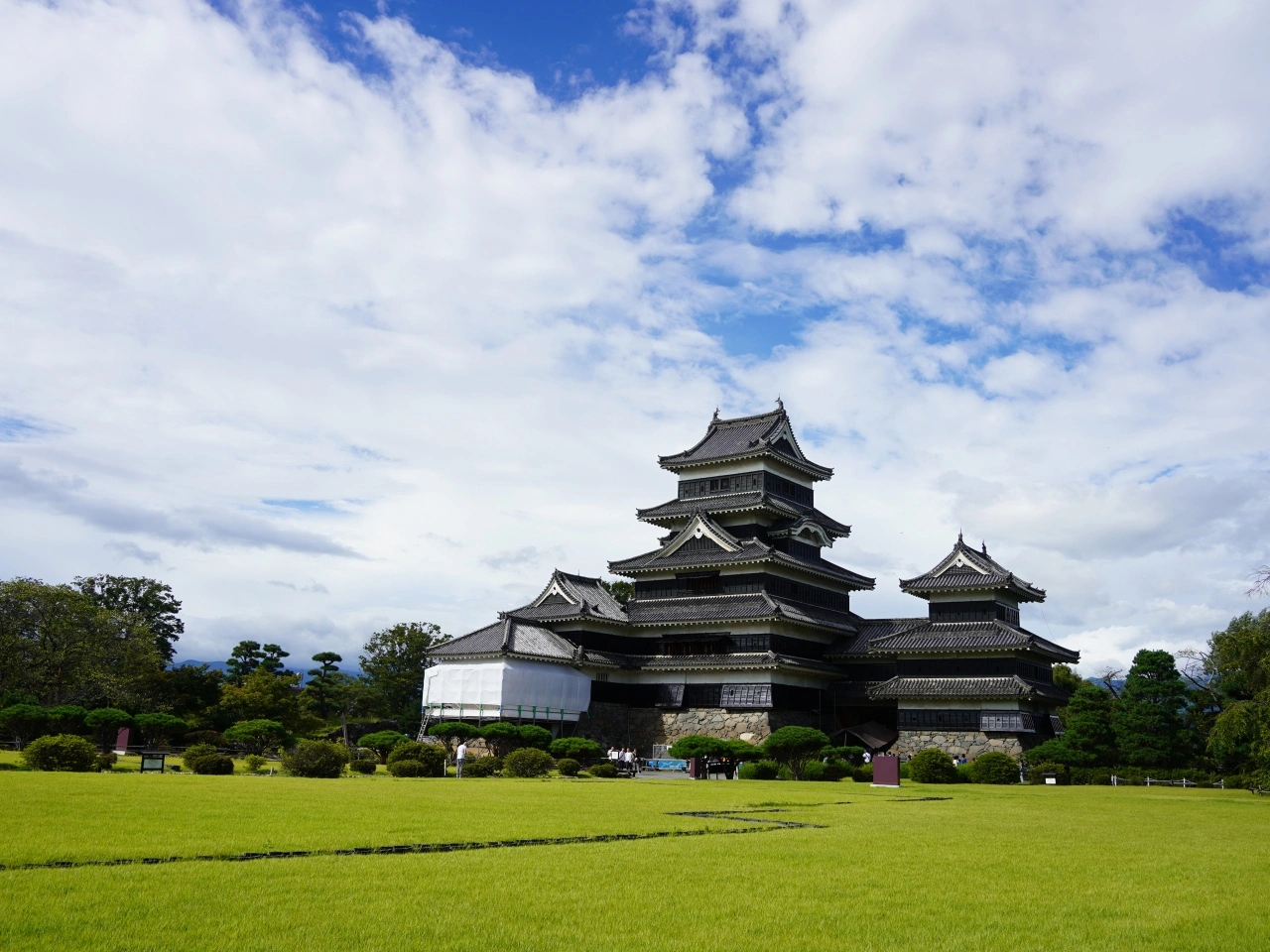晴天下壯麗的松本城，城堡外圍是廣闊的綠地和花園。